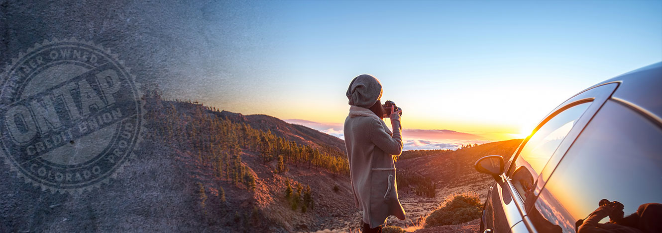 women viewing sunset with camera next to car