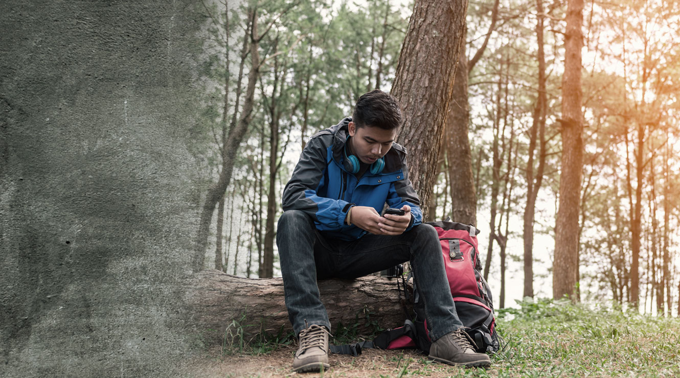 man sitting in woods looking at mobile phone